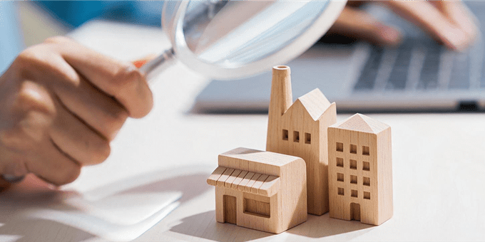 Une main tient une loupe au-dessus de maquettes en bois de bâtiments sur une table. Une main tient une loupe au-dessus de maquettes en bois de bâtiments sur une table.