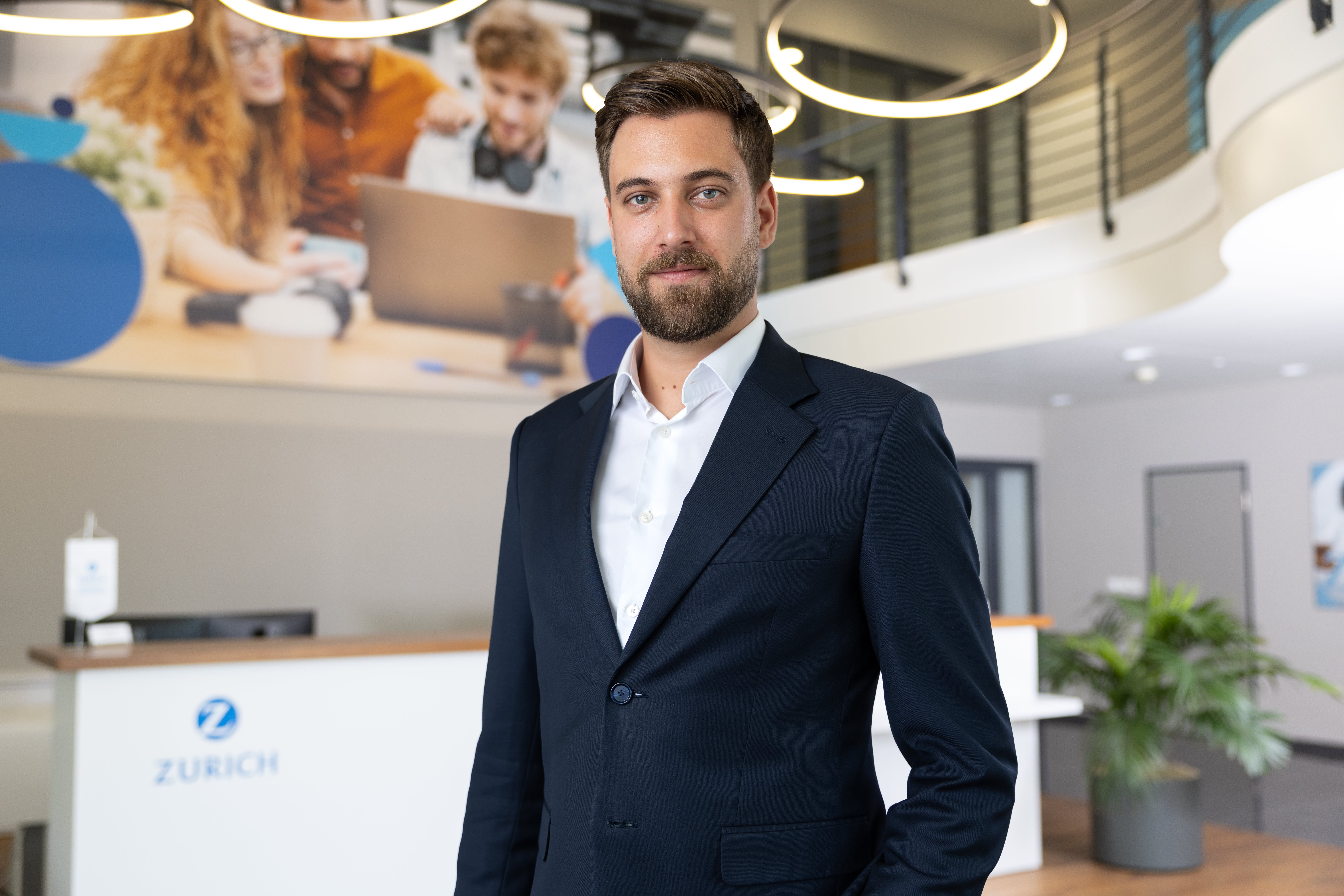 Ein Mann in einem Anzug steht in einem modernen Büro mit Pflanzen und einem Empfangstresen.