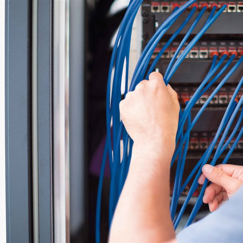 A hand is connecting blue cables in a server rack. A hand is connecting blue cables in a server rack.