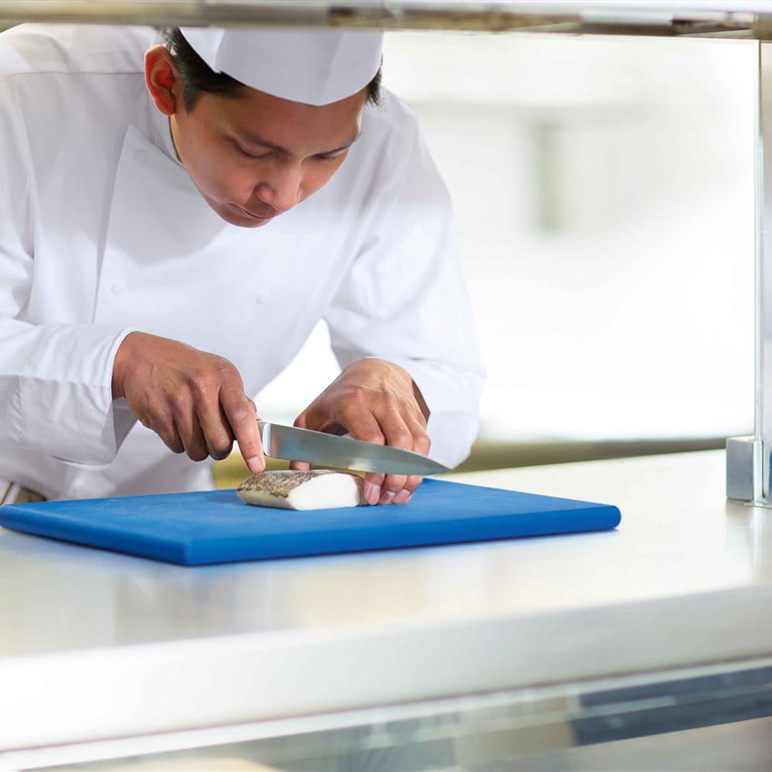 A chef is slicing fish on a blue cutting board. A chef is slicing fish on a blue cutting board.