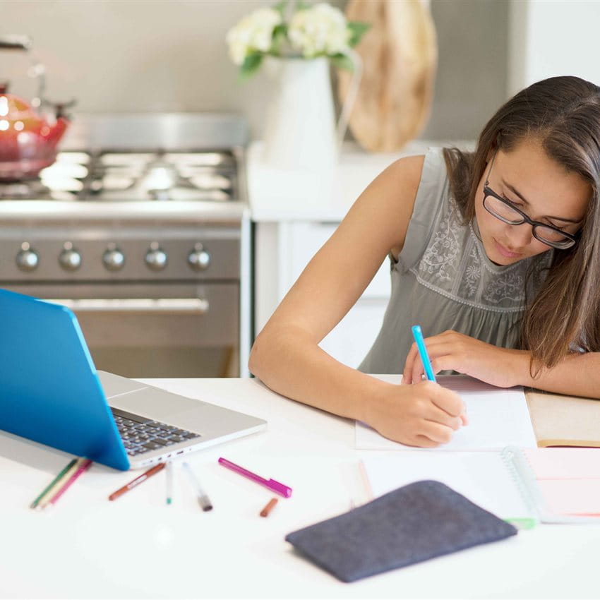 A girl is writing at a table with a laptop and writing supplies. A girl is writing at a table with a laptop and writing supplies.