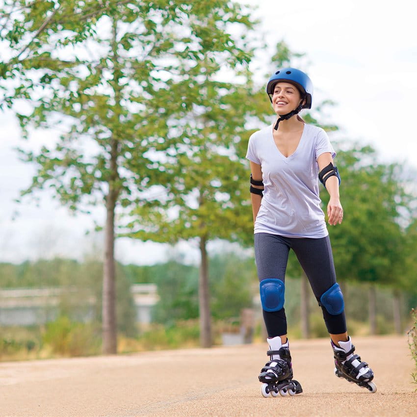 A woman wearing a helmet skates on a path with trees in the background. A woman wearing a helmet skates on a path with trees in the background.