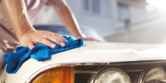 Une main avec un chiffon bleu nettoie le capot d'une voiture. Une main avec un chiffon bleu nettoie le capot d'une voiture.