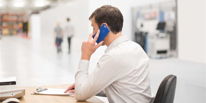A person on the phone sits at a desk in a large, bright hall. A person on the phone sits at a desk in a large, bright hall.