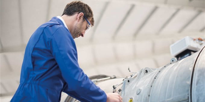 A person in a blue overall is performing maintenance on a large industrial machine. A person in a blue overall is performing maintenance on a large industrial machine.