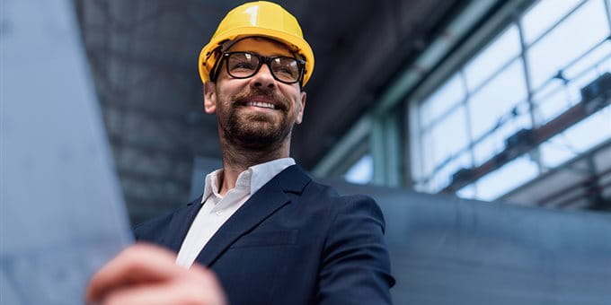 Uomo in un casco giallo e occhiali, sorride tenendo un piano in una stanza con grandi finestre. Uomo in un casco giallo e occhiali, sorride tenendo un piano in una stanza con grandi finestre.