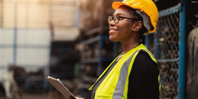 Une femme portant un casque de protection et un gilet réfléchissant tient un clipboard dans un entrepôt. Une femme portant un casque de protection et un gilet réfléchissant tient un clipboard dans un entrepôt.
