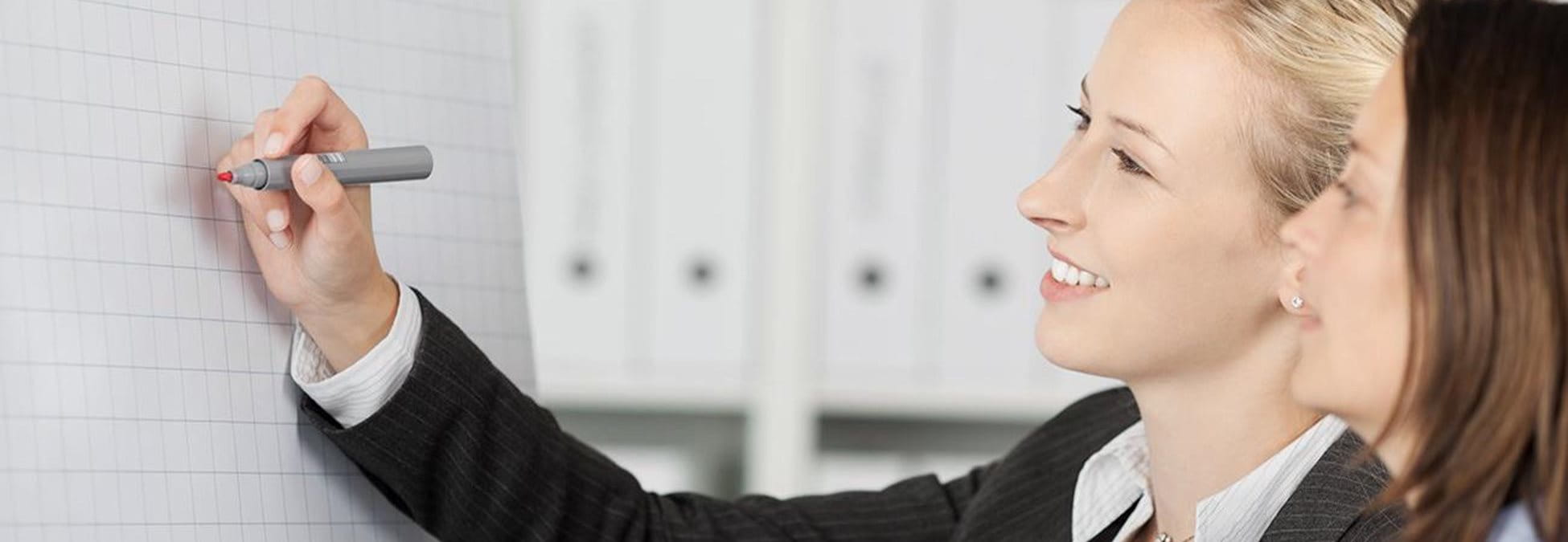 Deux femmes écrivent à un tableau blanc.