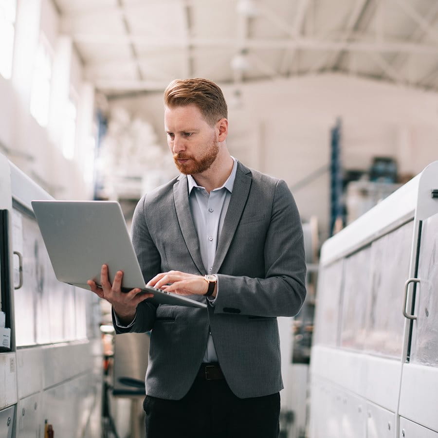 Un uomo in abbigliamento professionale lavora con un laptop in una sala industriale moderna, circondato da grandi macchinari.