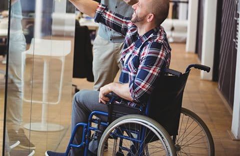 A man in a wheelchair sketches an idea with his work colleague on a glass wall in the office. A man in a wheelchair sketches an idea with his work colleague on a glass wall in the office.
