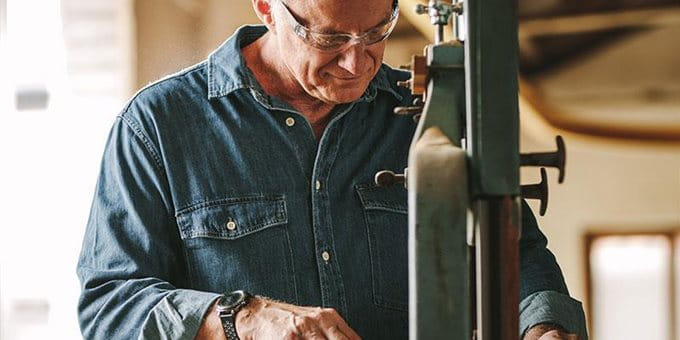 Ein älterer Mann in einem blauen Hemd arbeitet an einer Maschine in einer Werkstatt. Ein älterer Mann in einem blauen Hemd arbeitet an einer Maschine in einer Werkstatt.
