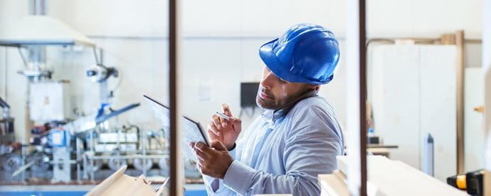 Un lavoratore con un casco blu tiene un tablet in un ambiente di lavorazione del legno. Un lavoratore con un casco blu tiene un tablet in un ambiente di lavorazione del legno.