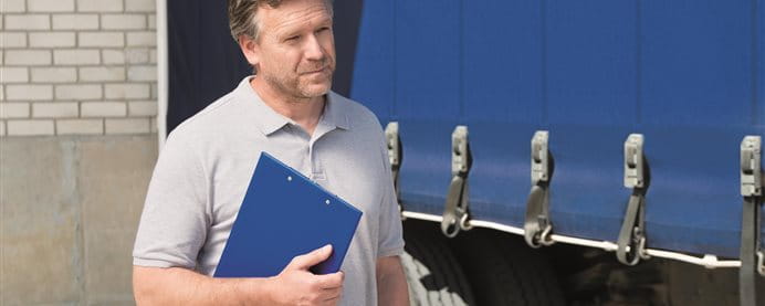 Uomo che tiene una clipboard blu di fronte a un camion. Uomo che tiene una clipboard blu di fronte a un camion.