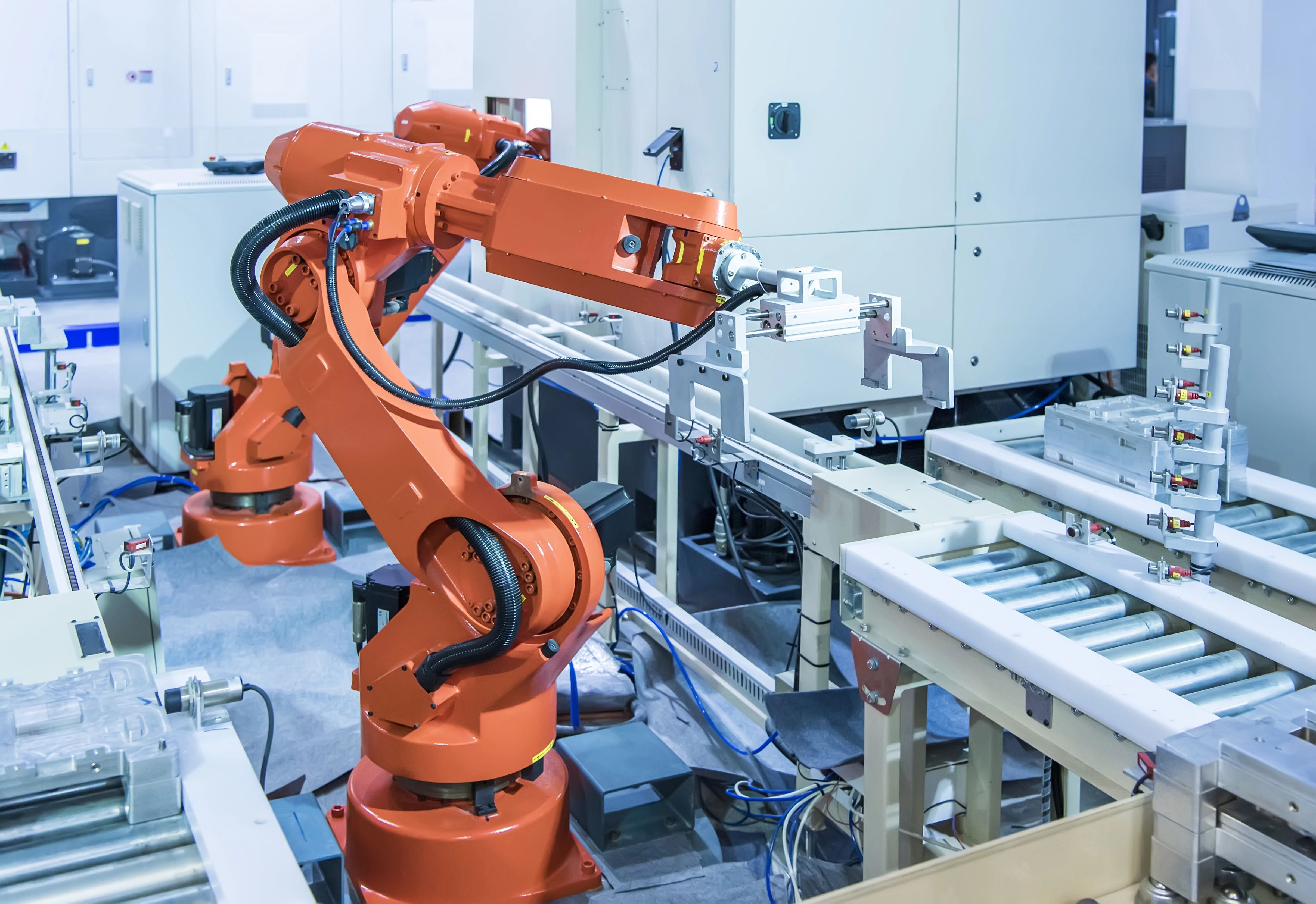Ein Roboterarm in einer industriellen Umgebung, der mit Förderbändern und Maschinen interagiert.