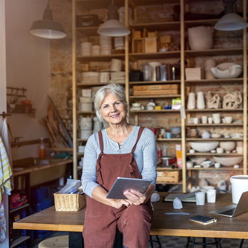 Una donna anziana è seduta con un tablet su un tavolo in uno spazio creativo. Una donna anziana è seduta con un tablet su un tavolo in uno spazio creativo.