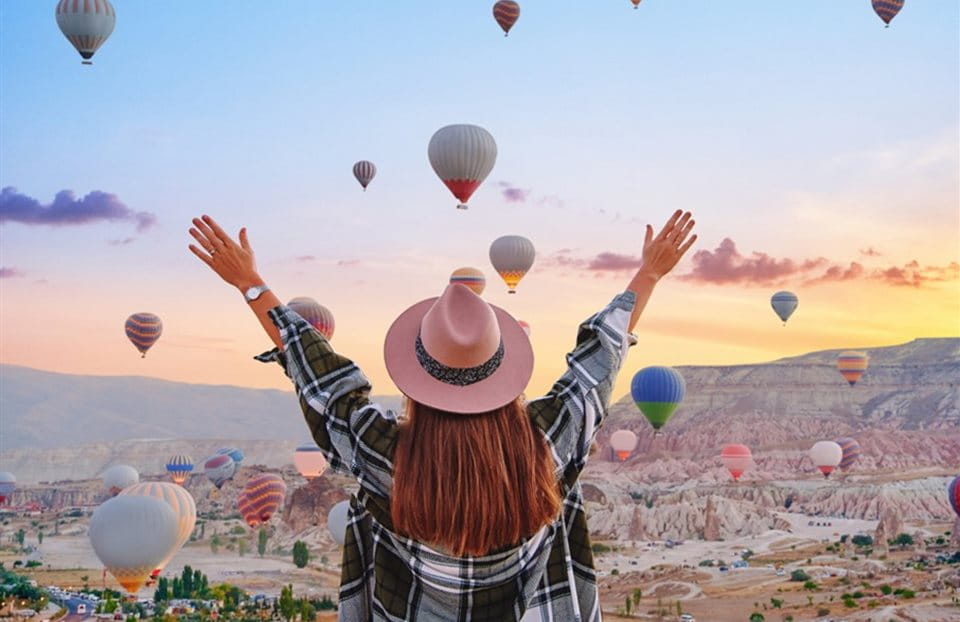Frau mit erhobenen Armen betrachtet viele Heissluftballons am Himmel bei Sonnenaufgang. Frau mit erhobenen Armen betrachtet viele Heissluftballons am Himmel bei Sonnenaufgang.