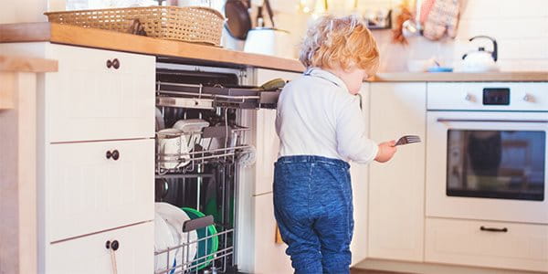 Un enfant se tient sur la porte du lave-vaisselle