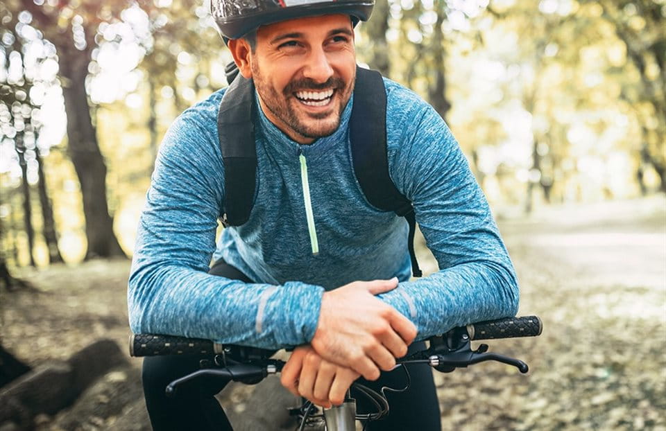 Un homme souriant en chemise bleue et casque sur un vélo dans la forêt. Un homme souriant en chemise bleue et casque sur un vélo dans la forêt.