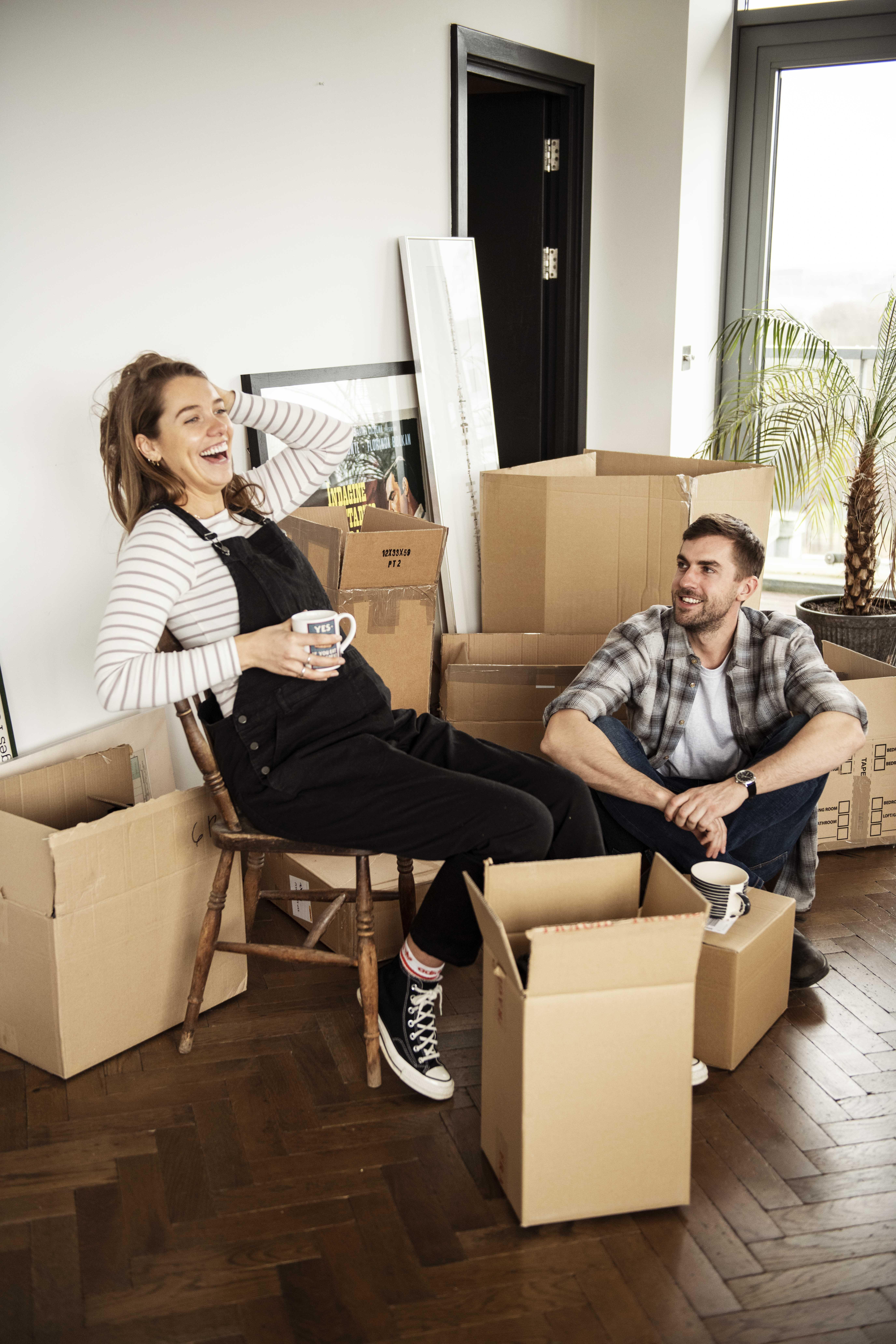 Schwangere Frau sitzend im Zimmer mit Mann am Boden und Umzugskisten