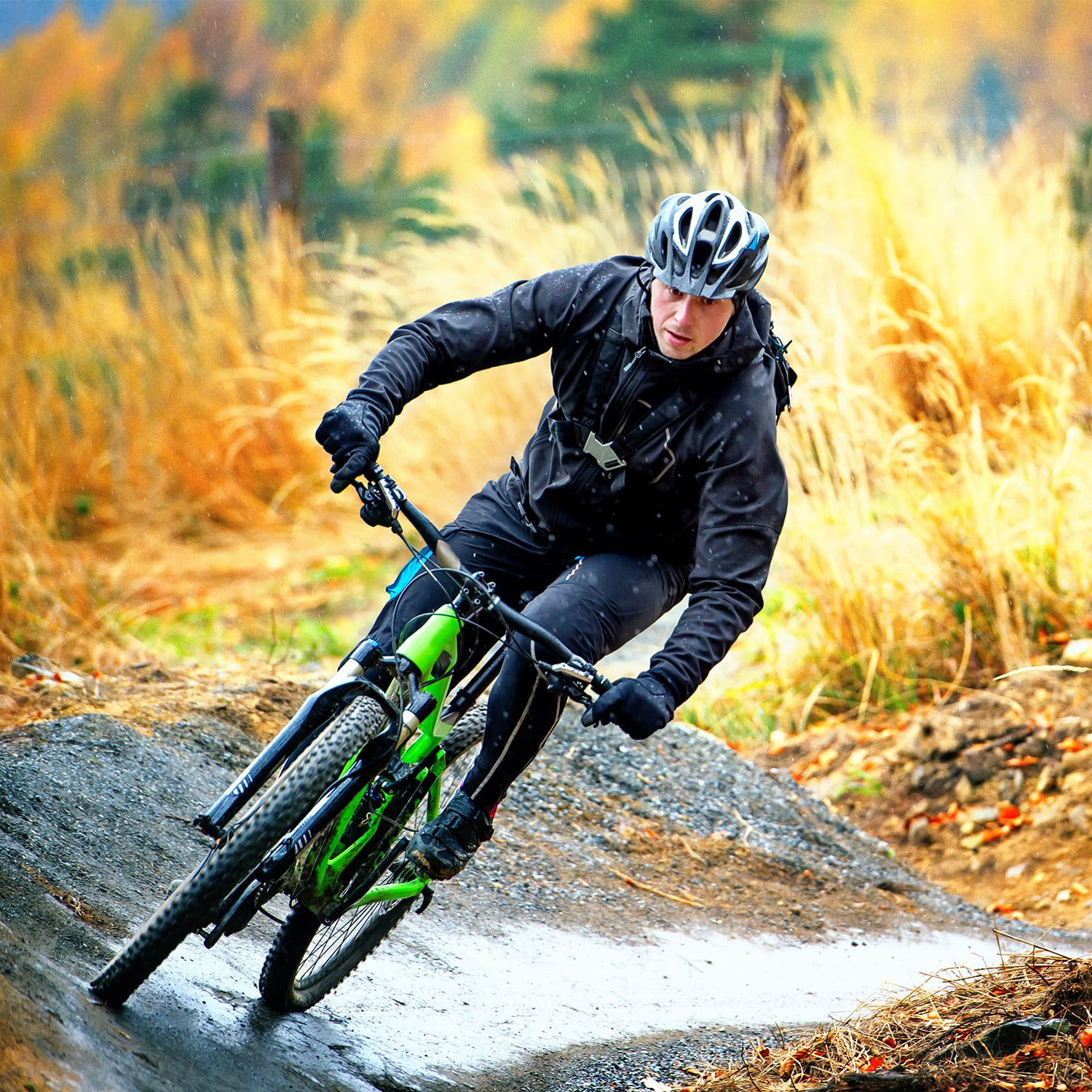 Une personne fait du vélo tout-terrain sur un chemin sinueux en plein air, entourée de paysages d'automne avec des herbes dorées et des arbres colorés.