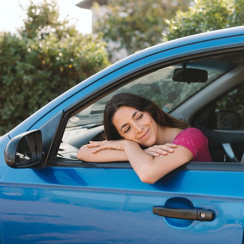Woman sitting in the driver's seat of a blue car, resting relaxed on the open window with her eyes closed. Woman sitting in the driver's seat of a blue car, resting relaxed on the open window with her eyes closed.