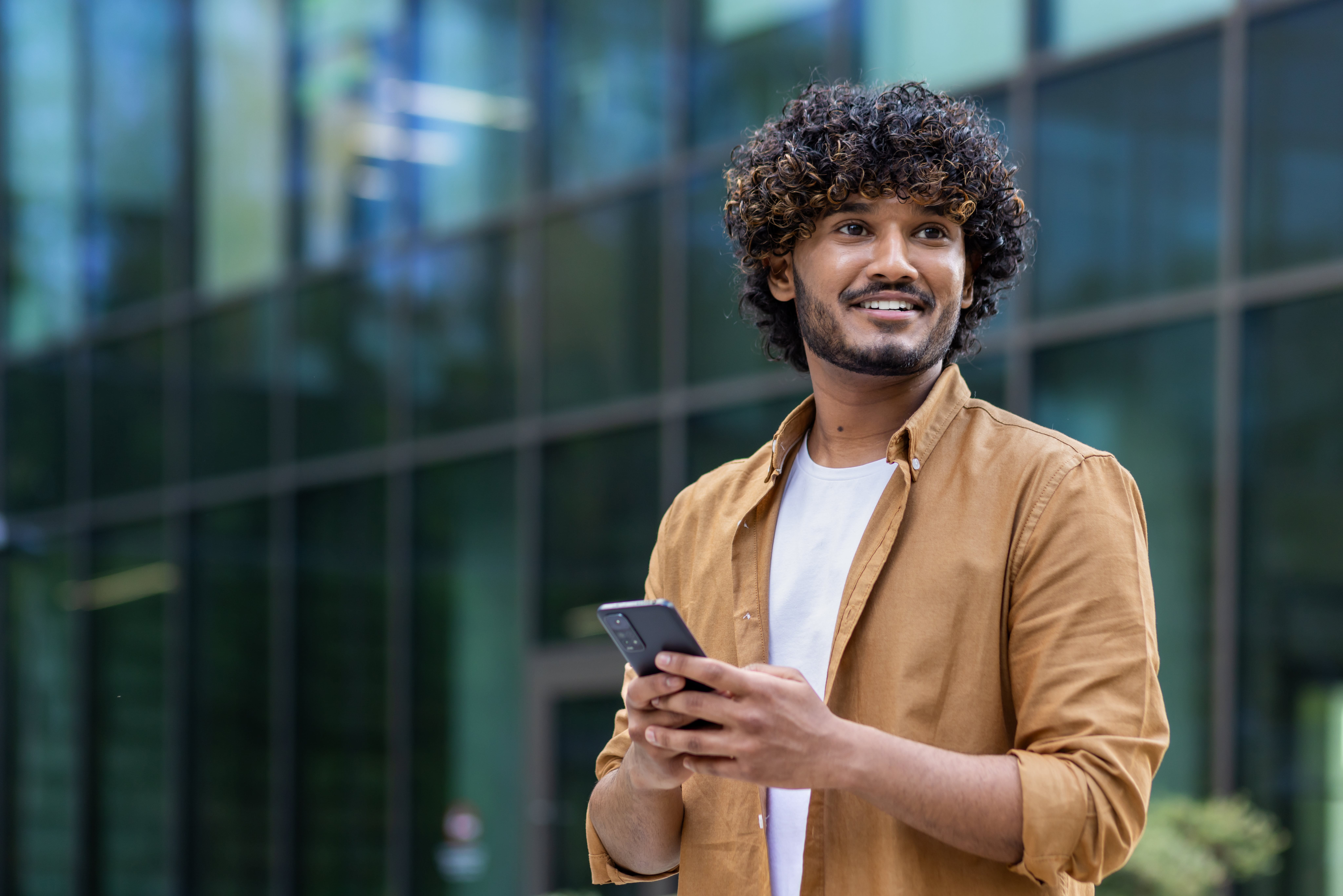 Personne debout devant un bâtiment moderne, tenant un smartphone.