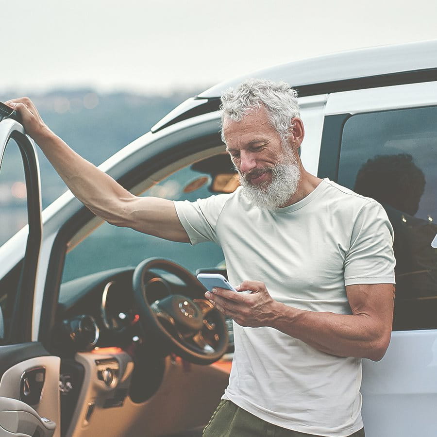 Mann lehnt am Auto mit Handy in der Hand