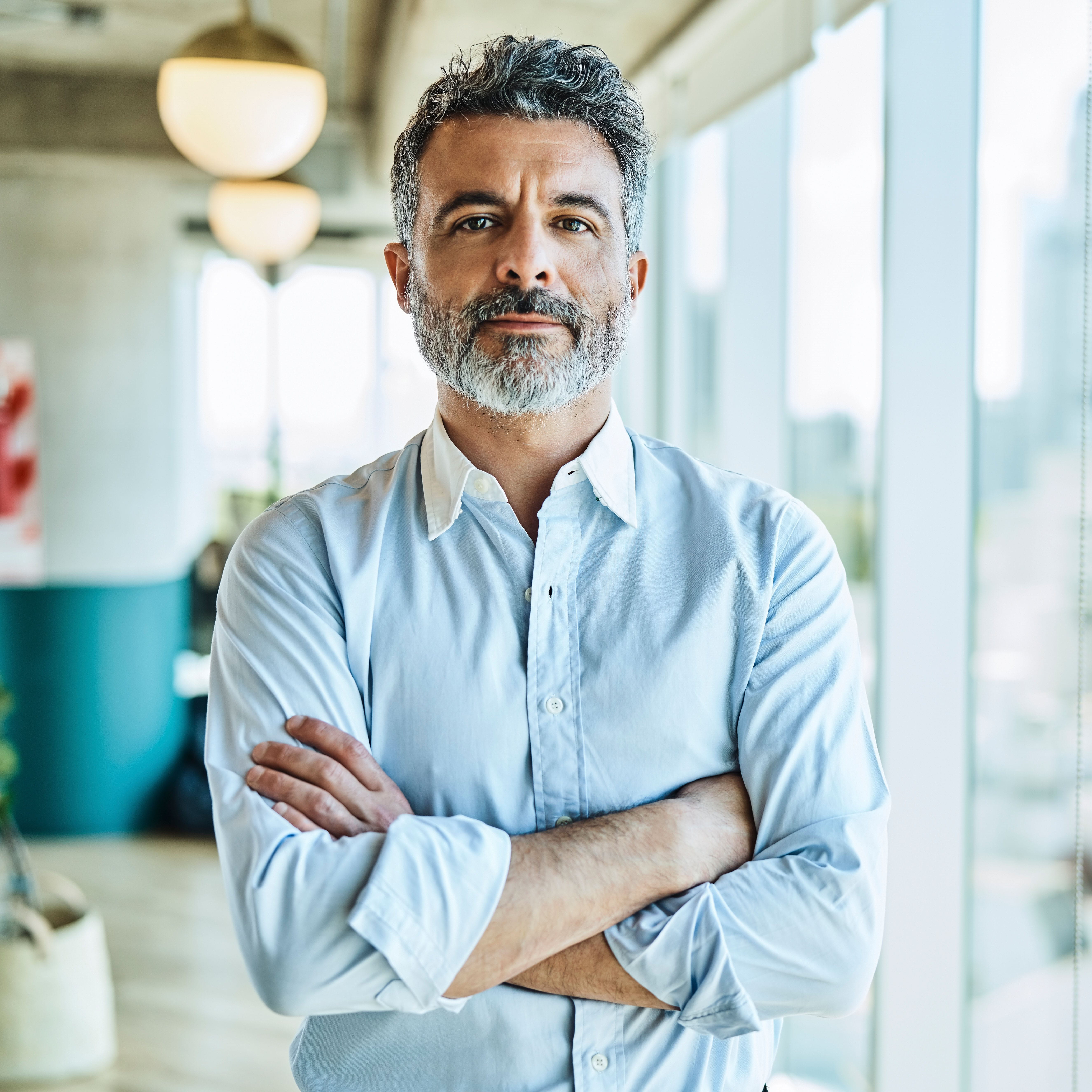 Ein Mann steht mit verschränkten Armen in einem modernen, hellen Büro mit grossen Fenstern.