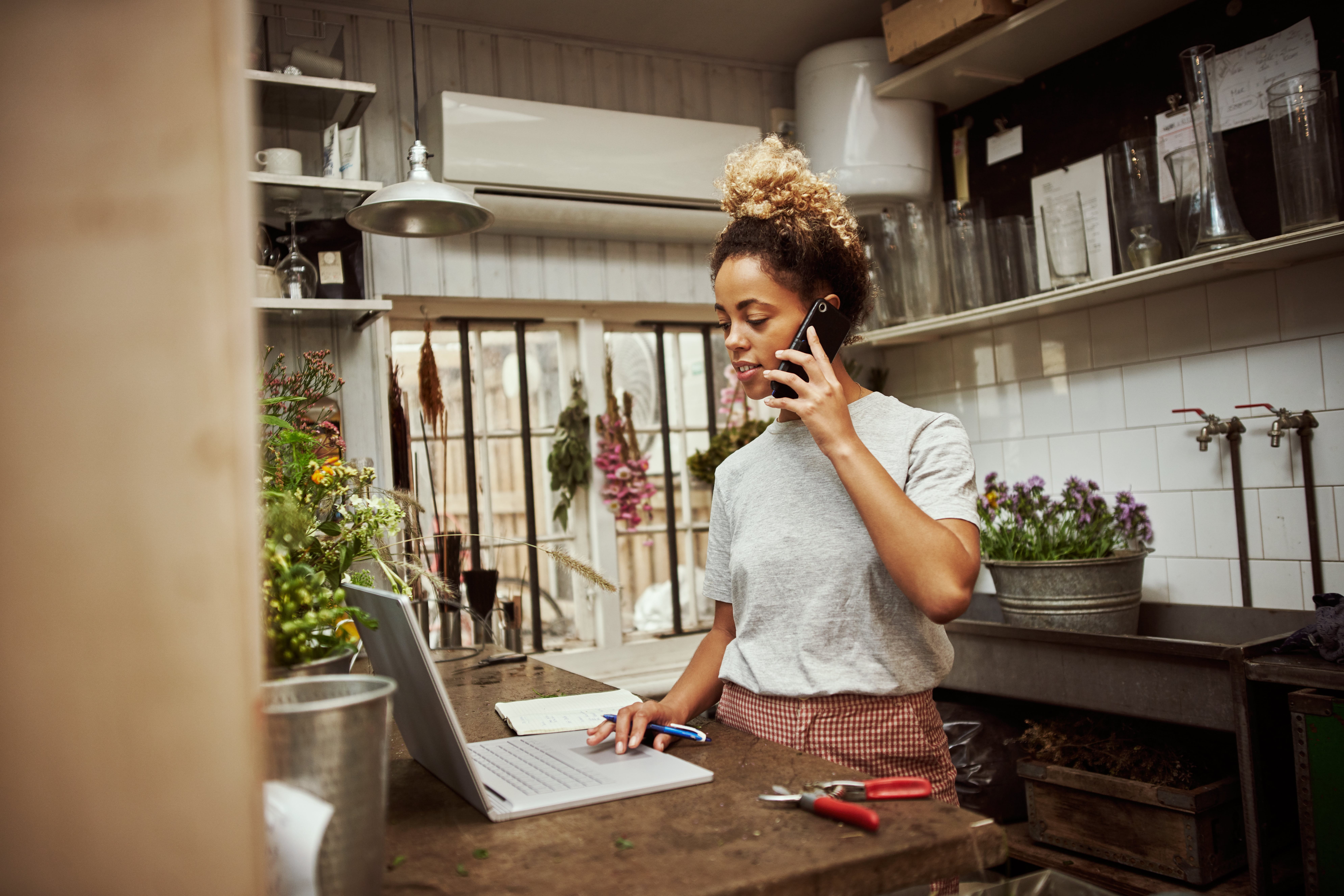 Frau arbeitet im Blumenladen am Laptop und Telefon.