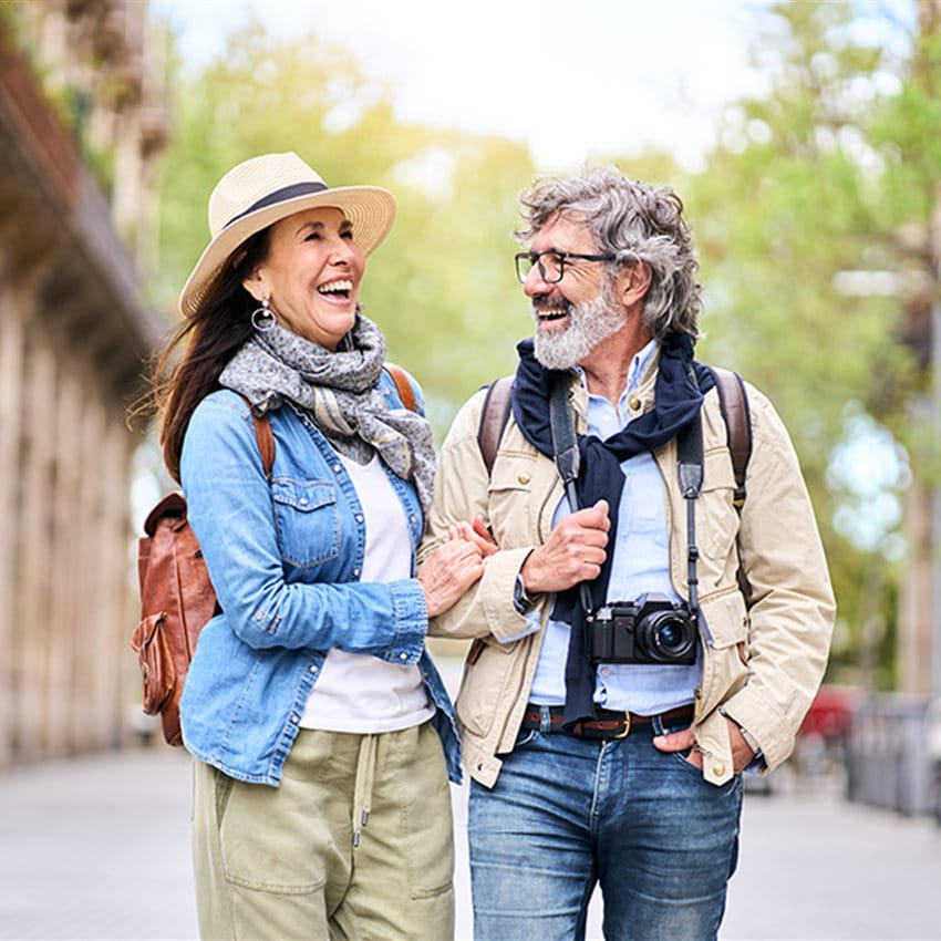 Zwei Personen spazieren gemeinsam durch eine Stadtallee. Sie tragen legere Kleidung, darunter Jacken und Schals, und haben Rucksäcke dabei. Eine Kamera hängt um den Hals einer Person. Die Umgebung wirkt entspannt und grün, im Hintergrund sind Gebäude und Bäume zu sehen. Zwei Personen spazieren gemeinsam durch eine Stadtallee. Sie tragen legere Kleidung, darunter Jacken und Schals, und haben Rucksäcke dabei. Eine Kamera hängt um den Hals einer Person. Die Umgebung wirkt entspannt und grün, im Hintergrund sind Gebäude und Bäume zu sehen.