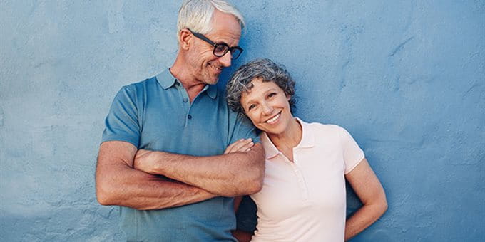 Un couple âgé se tient devant un mur bleu, s'appuie l'un contre l'autre et porte des vêtements d'été avec les bras croisés. Un couple âgé se tient devant un mur bleu, s'appuie l'un contre l'autre et porte des vêtements d'été avec les bras croisés.