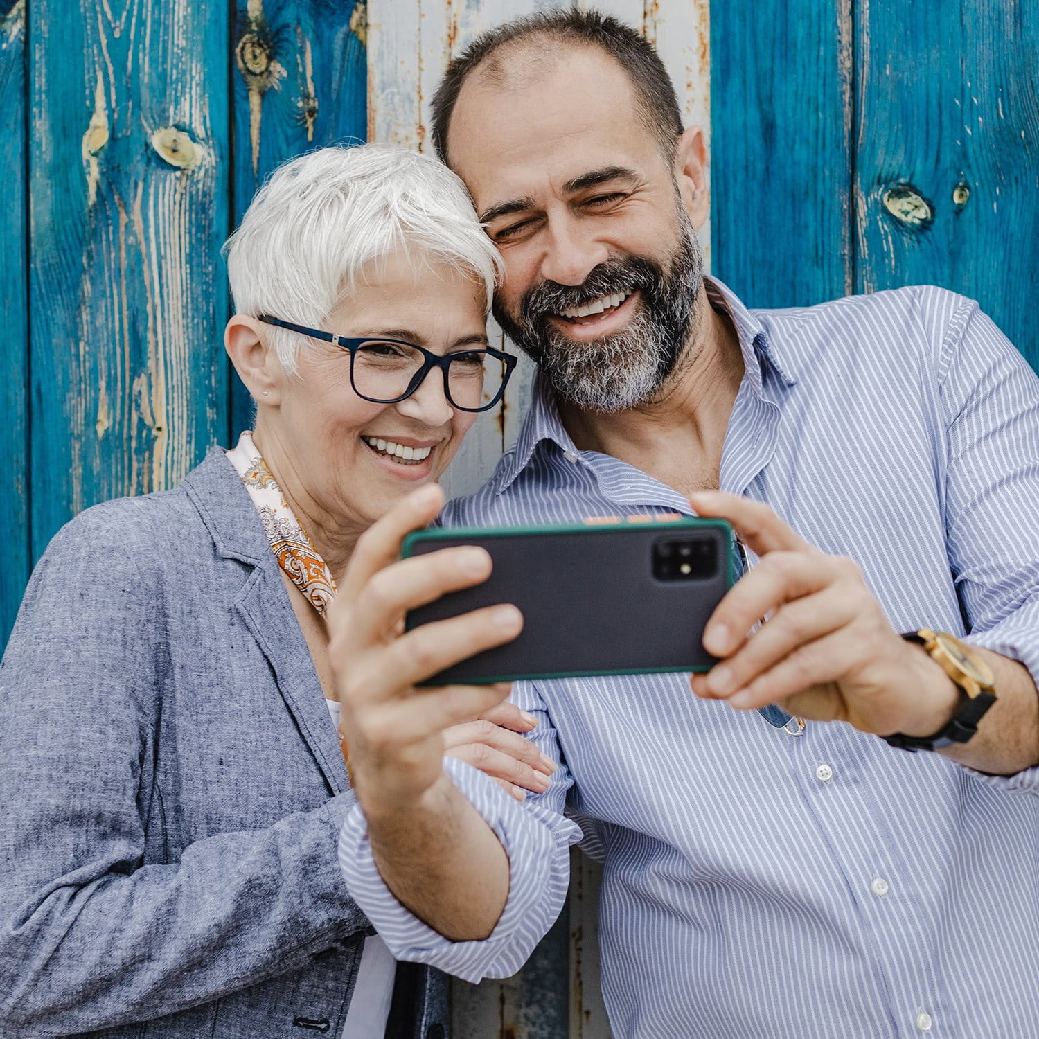 Una coppia sorride mentre fa un selfie davanti a una parete di legno.