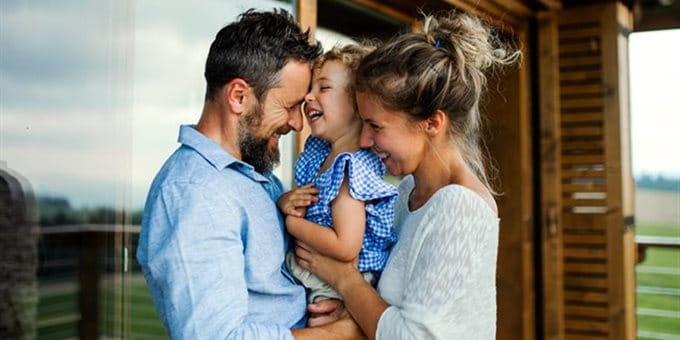 Una giovane famiglia abbracciata si trova su una terrazza davanti a una casa e si gode del tempo insieme all'aperto. Una giovane famiglia abbracciata si trova su una terrazza davanti a una casa e si gode del tempo insieme all'aperto.