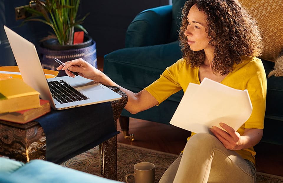 Une personne est assise avec un ordinateur portable, tenant des papiers et un stylo. Une personne est assise avec un ordinateur portable, tenant des papiers et un stylo.