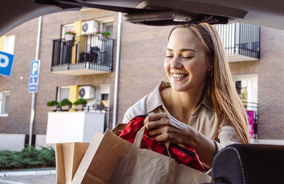 A woman smiles as she takes a bag from a car, with apartments in the background. A woman smiles as she takes a bag from a car, with apartments in the background.
