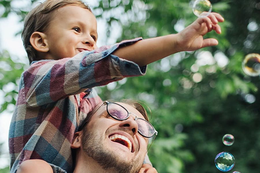 Un enfant assis sur les épaules de son père attrape des bulles de savon créées par sa mère.