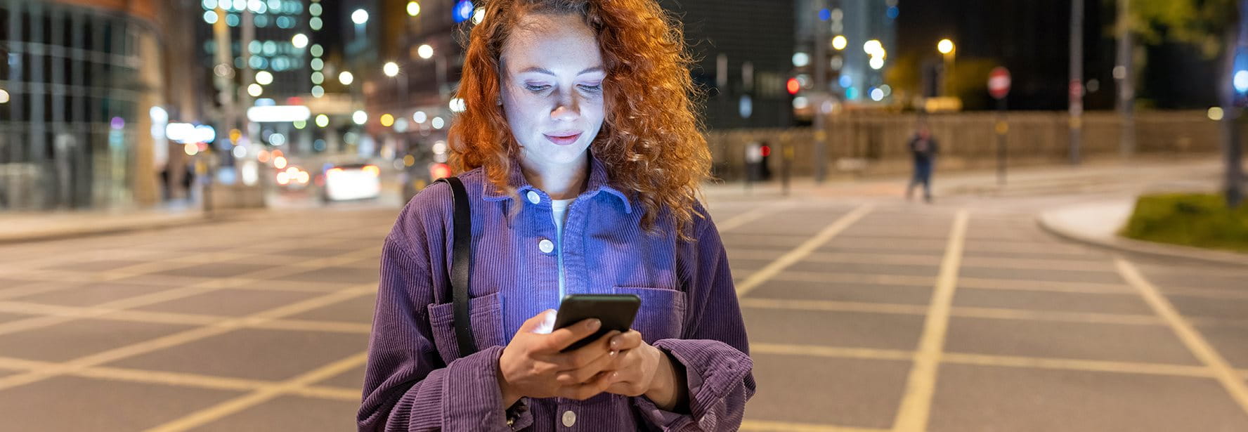 Donna in piedi in una piazza di sera e guarda il suo smartphone