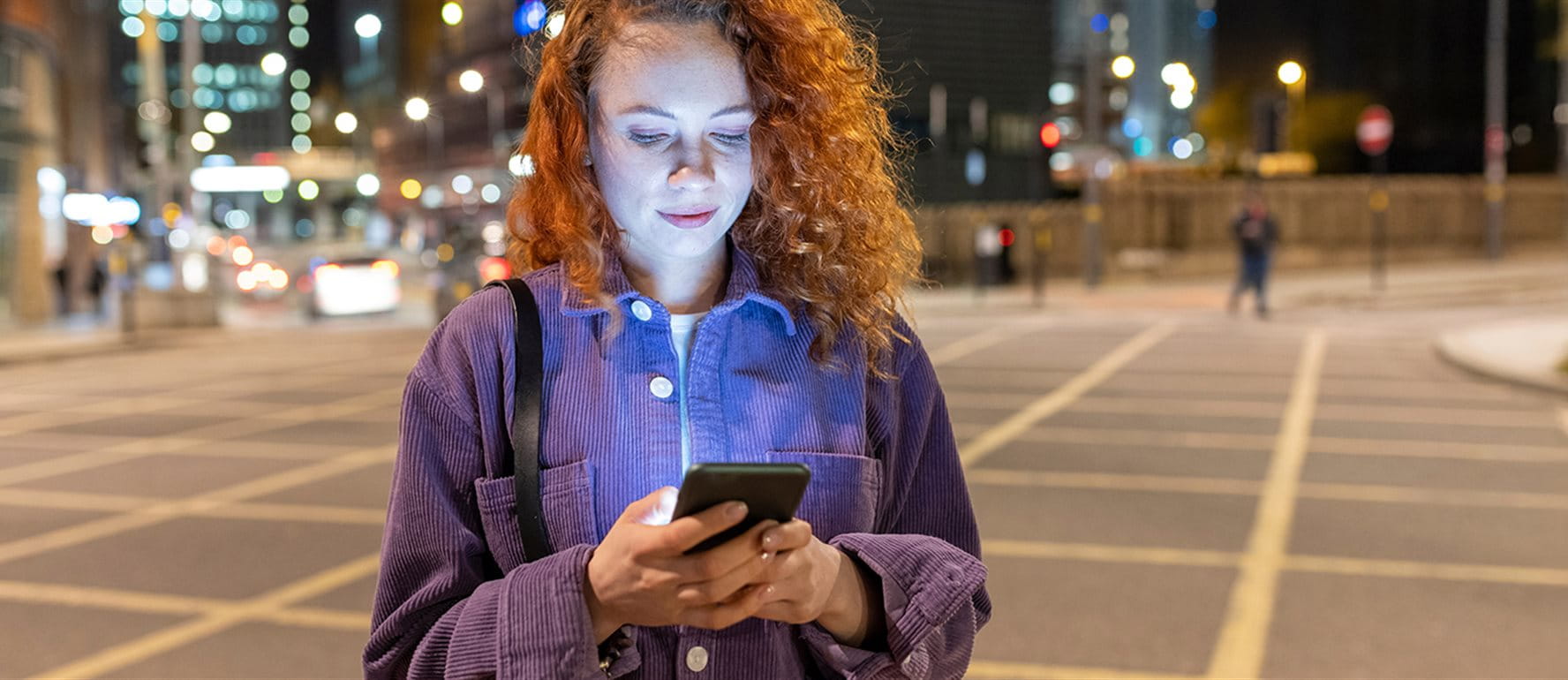 Frau steht am Abend auf einem Platz und sieht auf ihr Smartphone Frau steht am Abend auf einem Platz und sieht auf ihr Smartphone