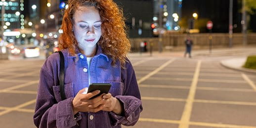 Woman stands in a square in the evening and looks at her smartphone
