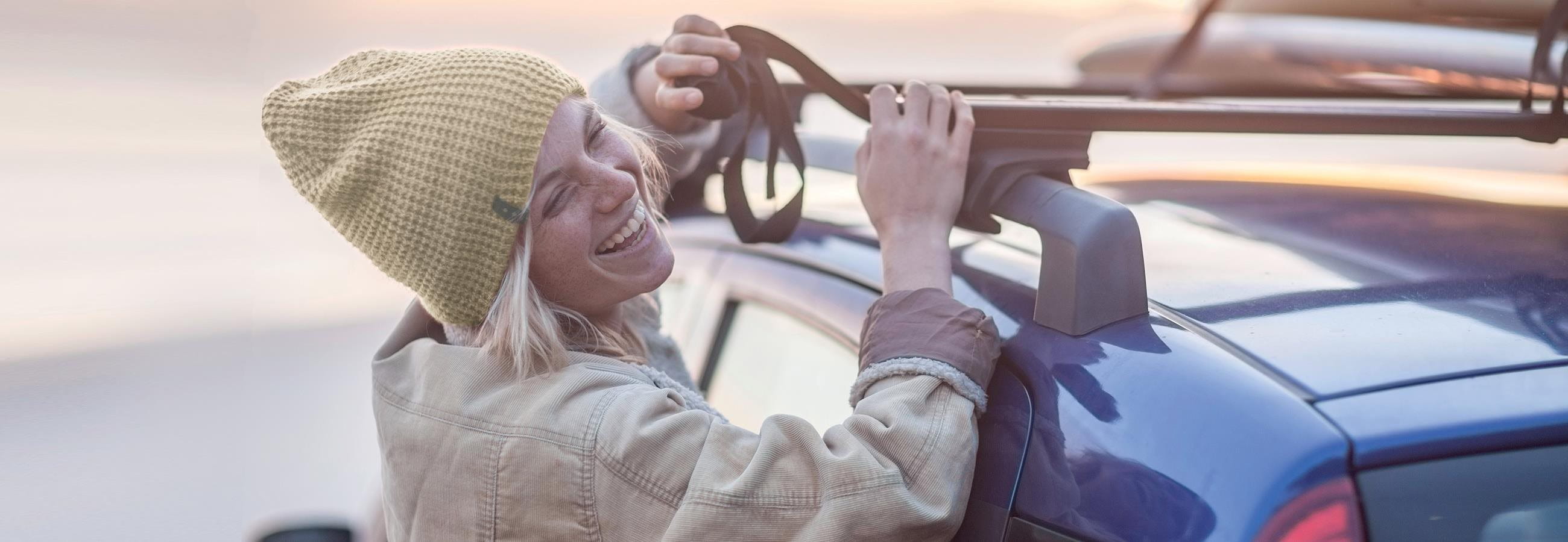 Junge Frau befestigt Surfbrett auf dem Autodache Junge Frau befestigt Surfbrett auf dem Autodache
