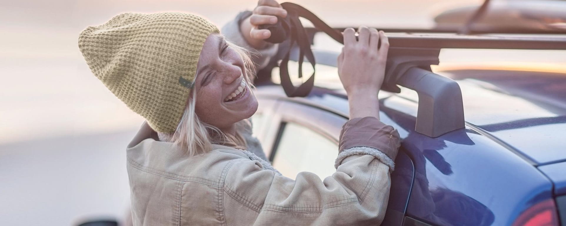 Junge Frau befestigt Surfbrett auf dem Autodache Junge Frau befestigt Surfbrett auf dem Autodache