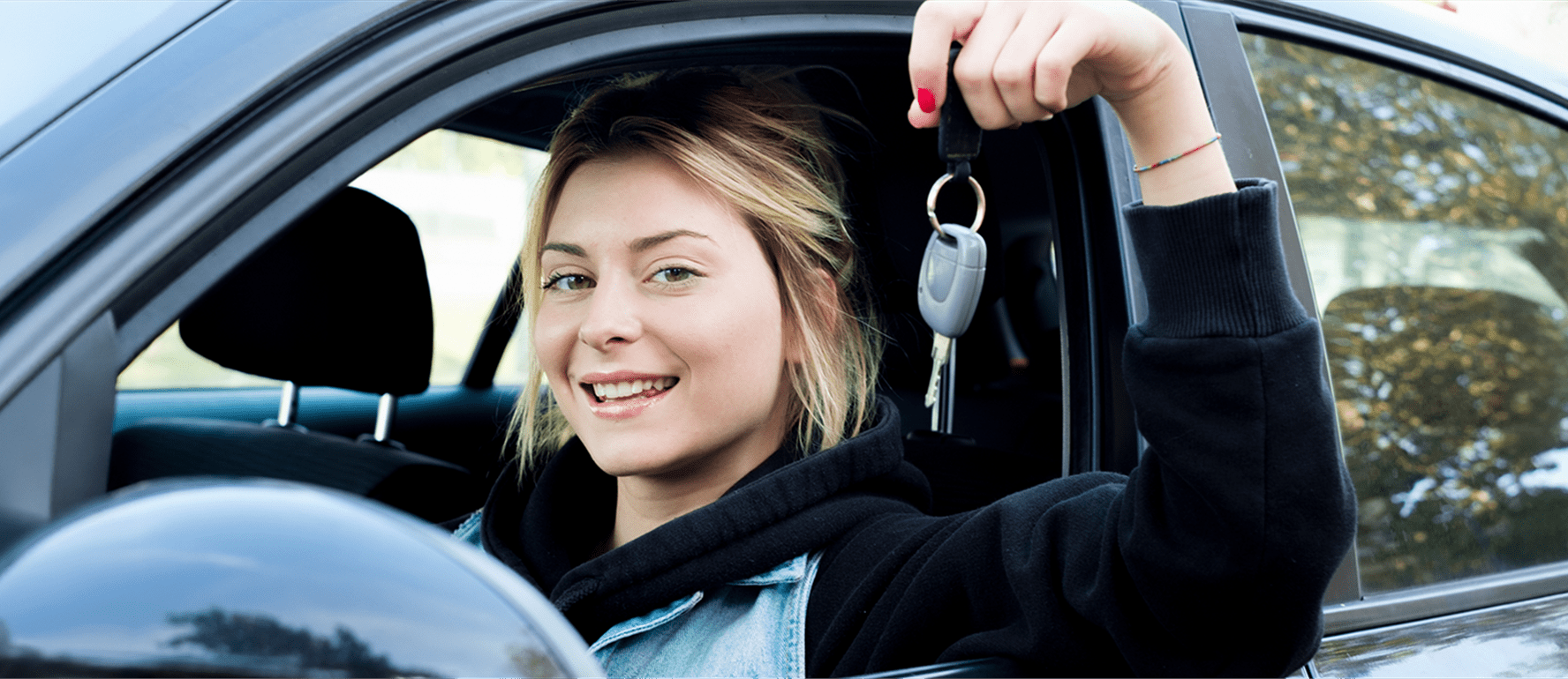 Una donna siede in macchina e mostra le chiavi dell'auto dal finestrino Una donna siede in macchina e mostra le chiavi dell'auto dal finestrino