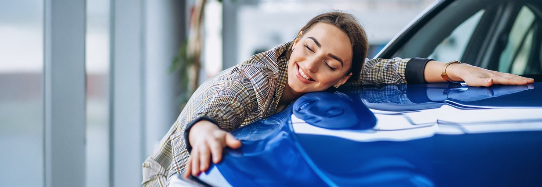 Une femme étreint joyeusement une voiture bleue. Elle sourit et semble satisfaite.