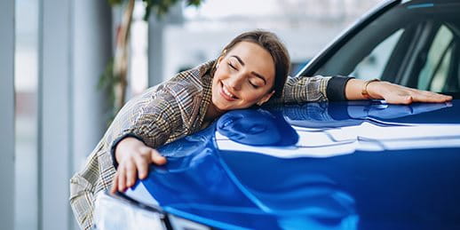 Une femme étreint avec enthousiasme le capot d'une voiture bleue.