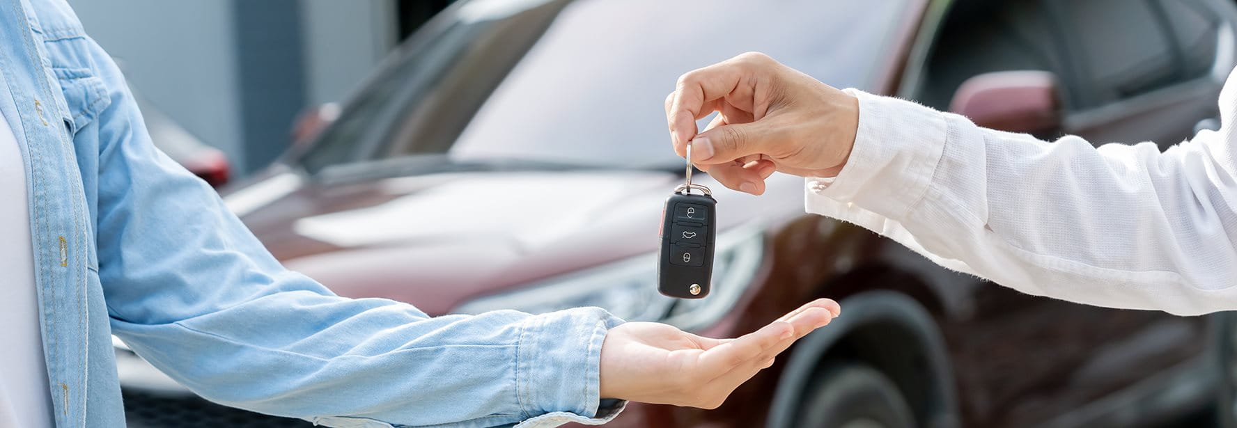 Une personne remet les clés d’une voiture à une autre devant une voiture garée