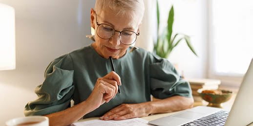 Woman sitting in front of a laptop with pen and paper
