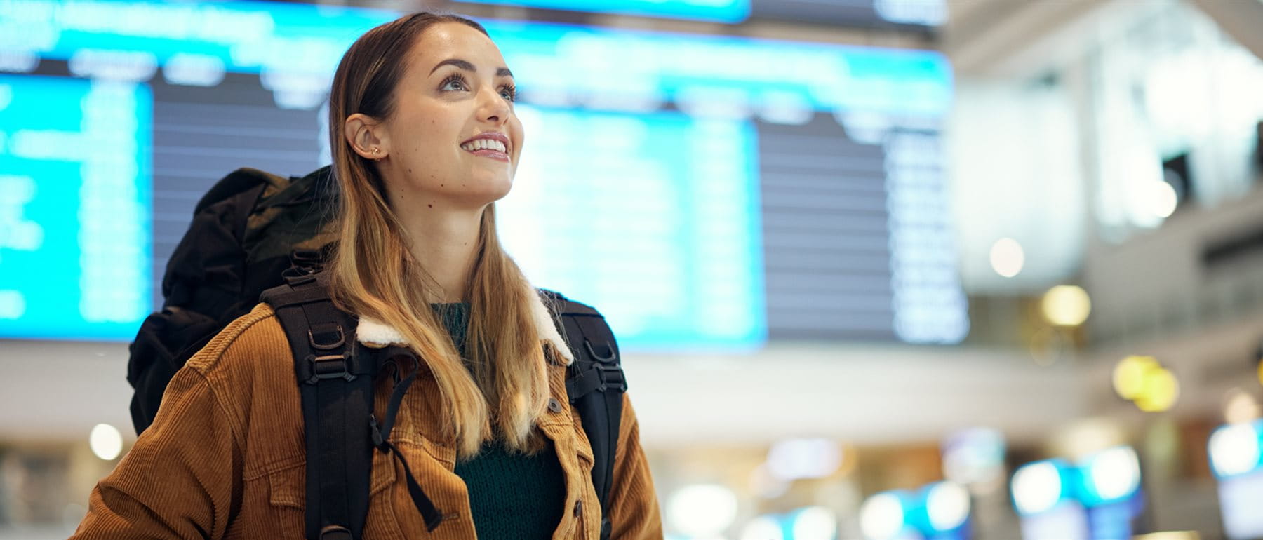 Eine junge Frau mit Rucksack steht am Flughafen und hält Reisedokumente in der Hand. Im Hintergrund sind Abflugtafeln und das geschäftige Flughafenumfeld zu sehen. Eine junge Frau mit Rucksack steht am Flughafen und hält Reisedokumente in der Hand. Im Hintergrund sind Abflugtafeln und das geschäftige Flughafenumfeld zu sehen.