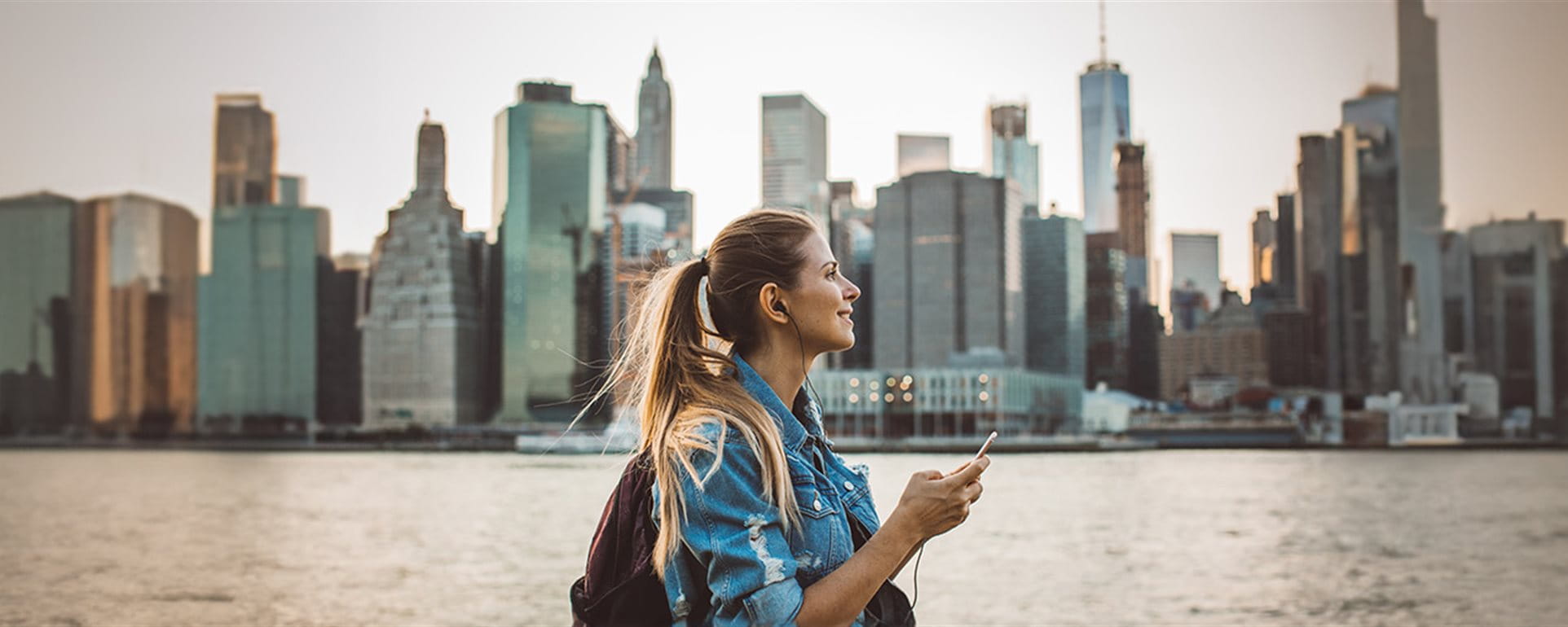 A person stands by the water, looking at a city skyline filled with tall buildings in the background. A person stands by the water, looking at a city skyline filled with tall buildings in the background.