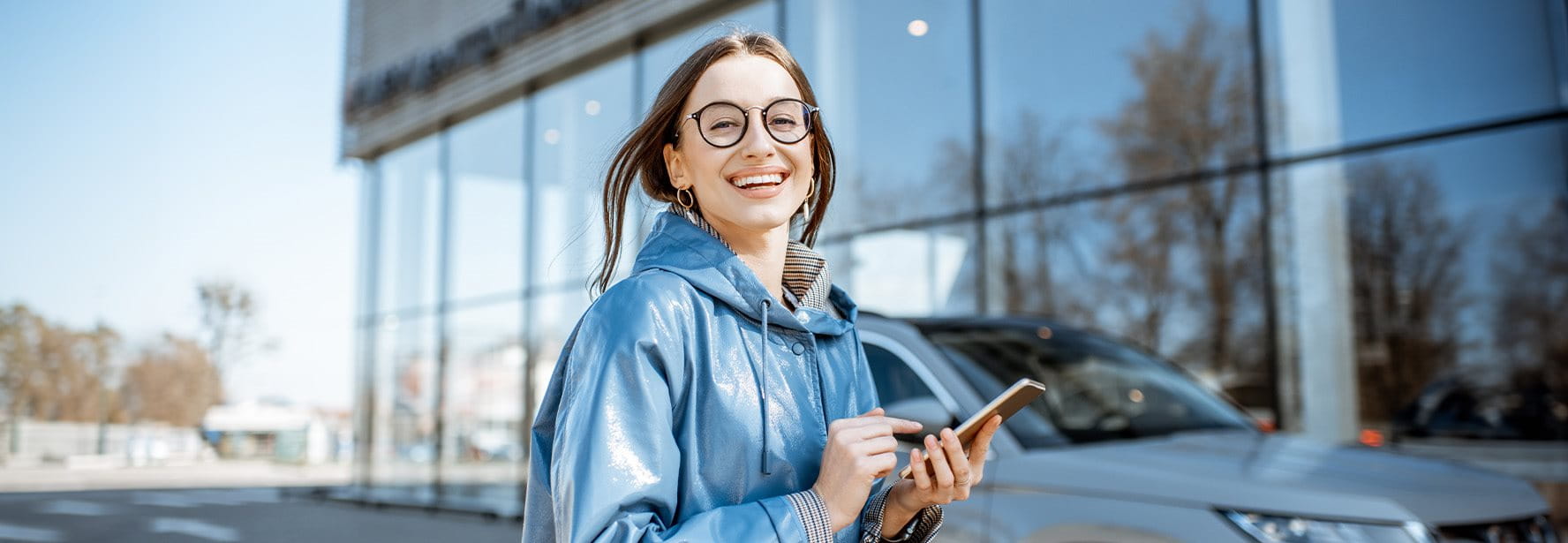 A woman stands in front of a car and types something into her smartphone