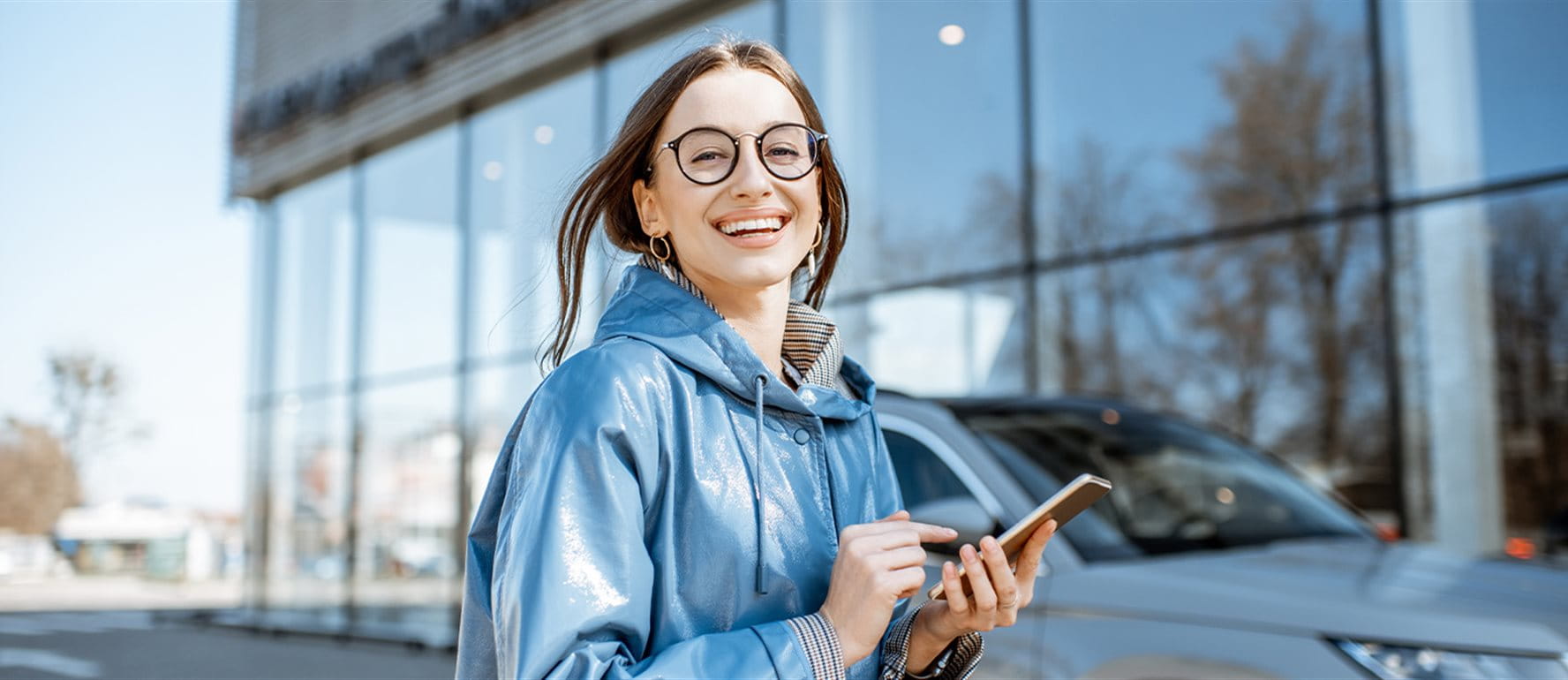 Eine Frau steht vor einem Auto und gibt etwas in ihr Smartphone ein Eine Frau steht vor einem Auto und gibt etwas in ihr Smartphone ein